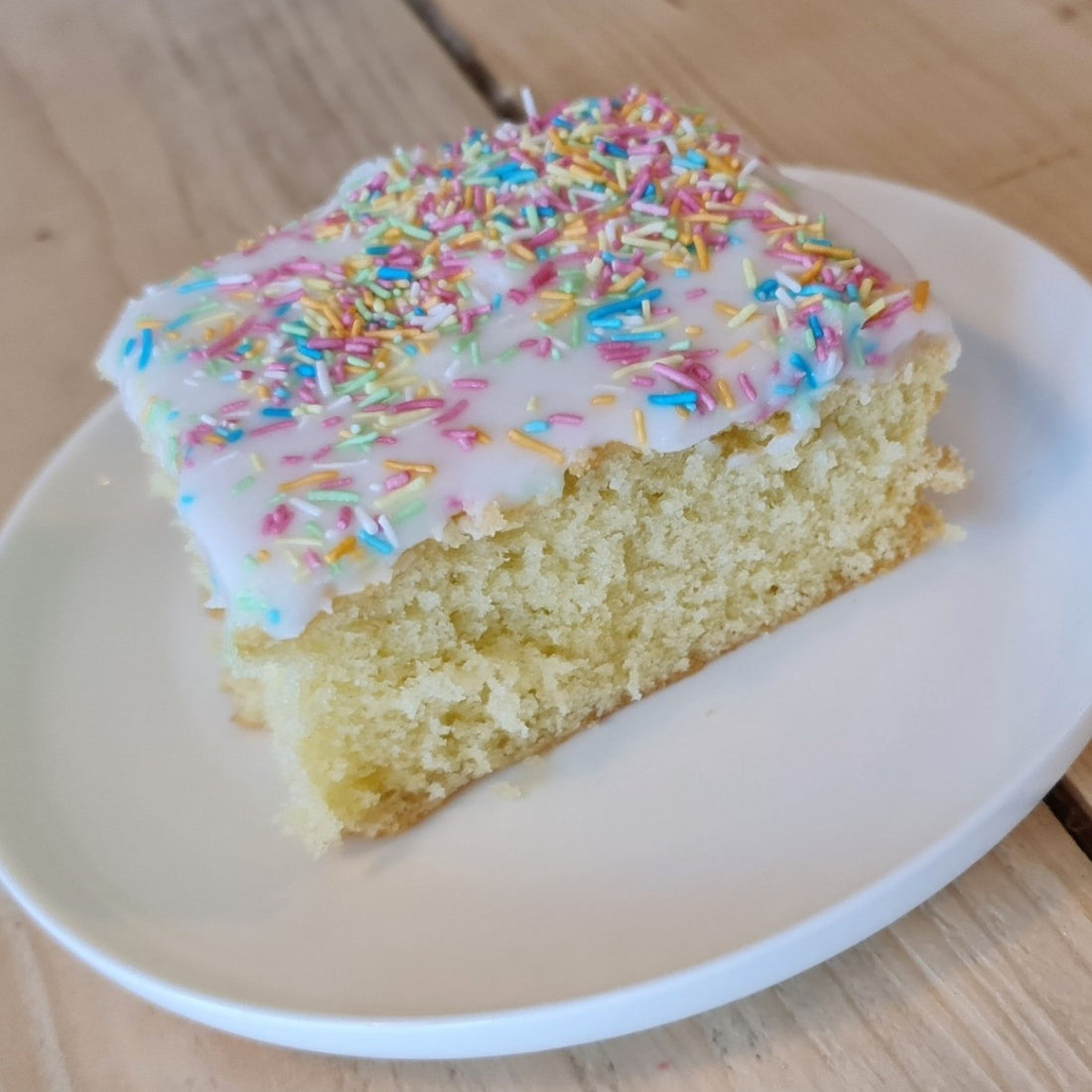 Old  school cake sponge cake square slice on a plate, well lit on a wooden table, clear clean appearance